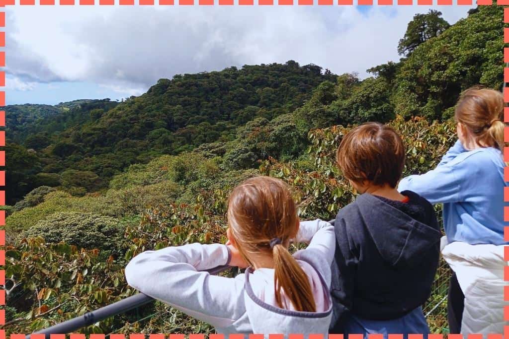 Sofi, Ian y Vicky de espaldas en un puente colgante, admirando el impresionante paisaje desde las copas de los árboles en el Bosque Nuboso Monteverde.