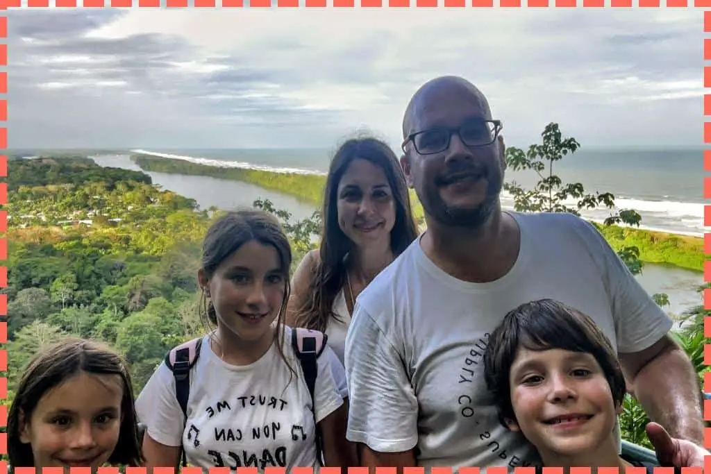 Familia sonriente y satisfecha en la cima del sendero El Cerro en Tortuguero, Costa Rica, con vistas panorámicas de los canales serpenteantes y el mar Caribe en la distancia.