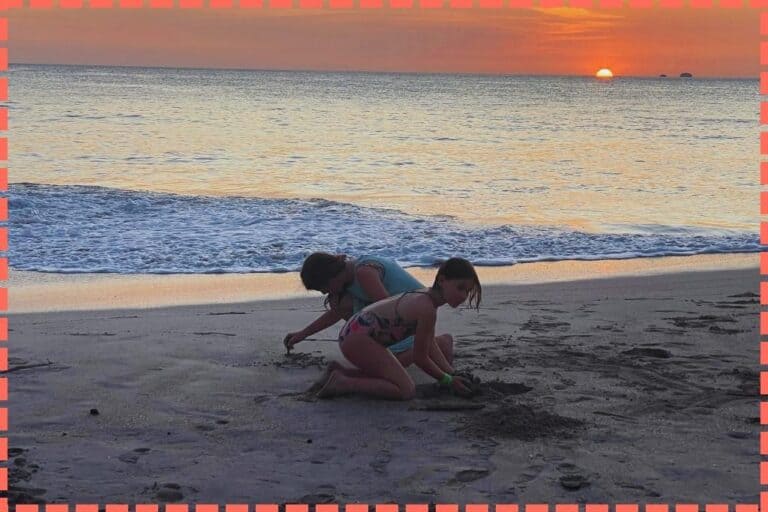 Dos niñas disfrutan jugando en la arena de Playa Flamingo Guanacaste Costa Rica, con un atardecer espectacular de fondo.