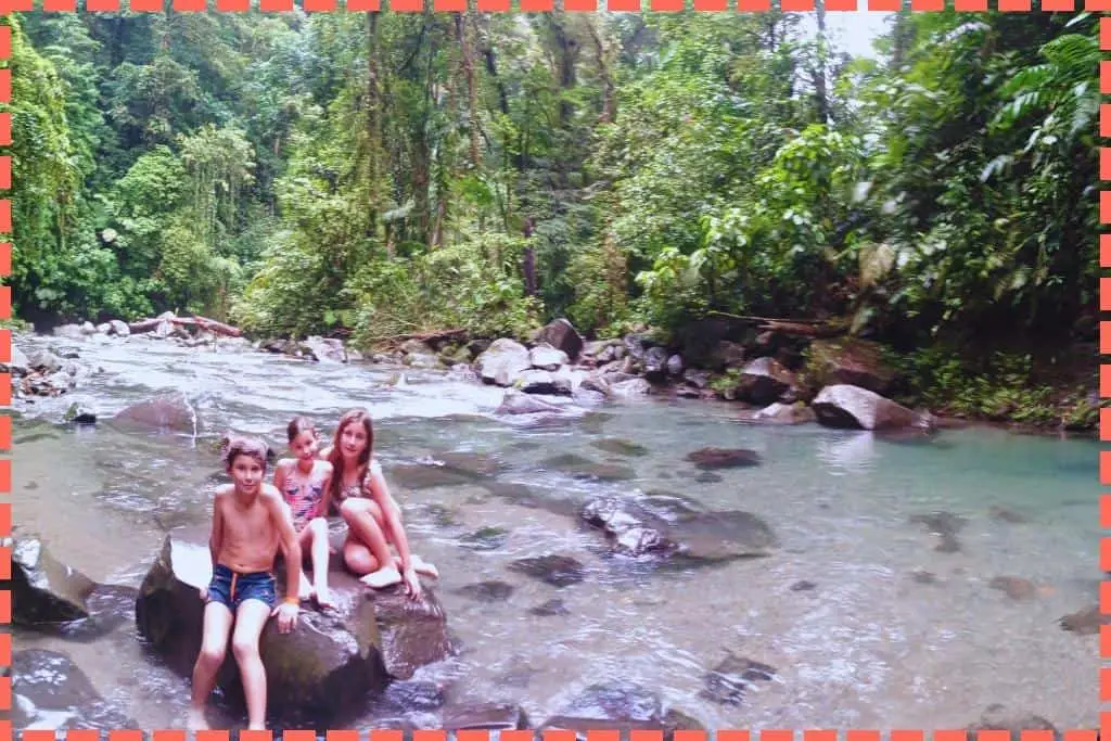 Sofi, Ian y Vicky sobre una piedra en las aguas del río que fluye desde la Catarata La Fortuna.