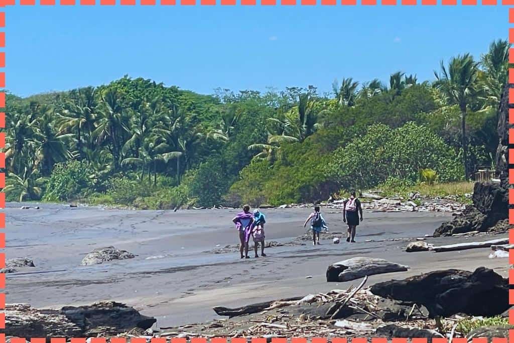 Familia caminando por Playa Azul, Costa Rica, con arena negra, vegetación densa y palmeras como telón de fondo
