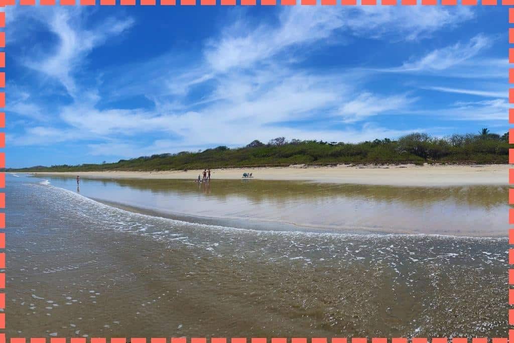 Fotografía panorámica de la hermosa Playa Grande con una familia disfrutando a lo lejos en la orilla.