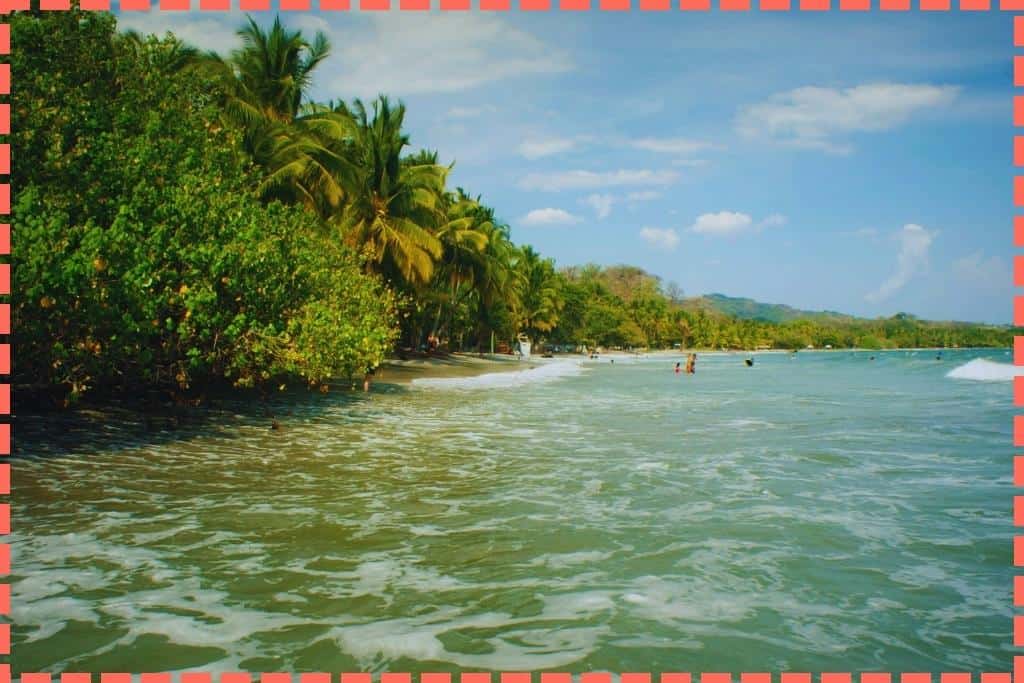 magen de Playa Sámara en Costa Rica, donde el mar besa la abundante vegetación mientras personas disfrutan de un baño al fondo