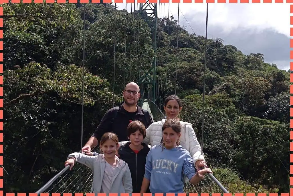 Familia de 5 personas caminando sobre un puente colgante en La Fortuna, Costa Rica, con el bosque nuboso debajo.