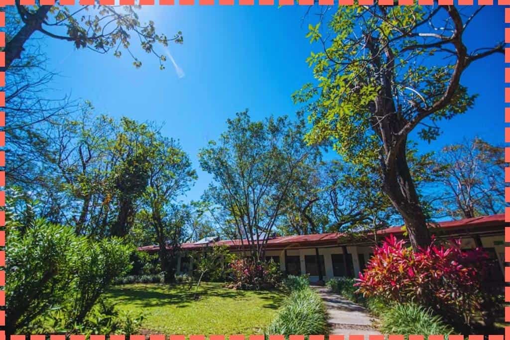 Exterior de las habitaciones del Hotel Guachipelin en Rincón de la Vieja, Costa Rica, mostrando su jardín de vegetación colorida en un día de cielo azul radiante.
