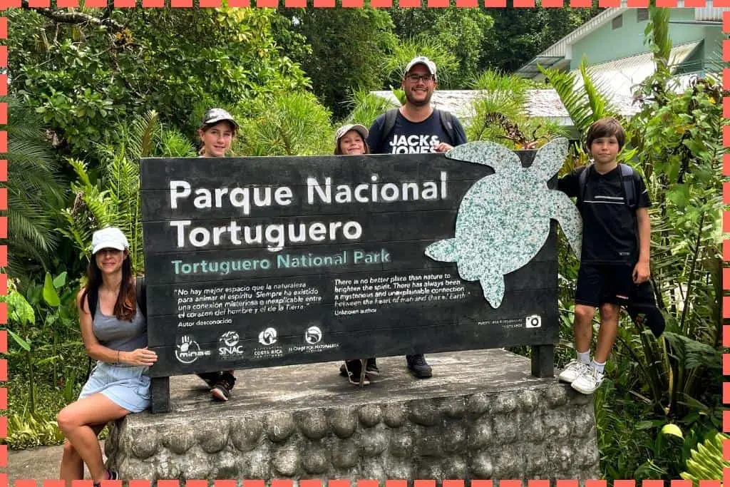 Una familia sonriente sosteniendo un cartel del Parque Nacional Tortuguero en Costa Rica, posando para la cámara con expresiones de felicidad y expectativa por la aventura que les espera.