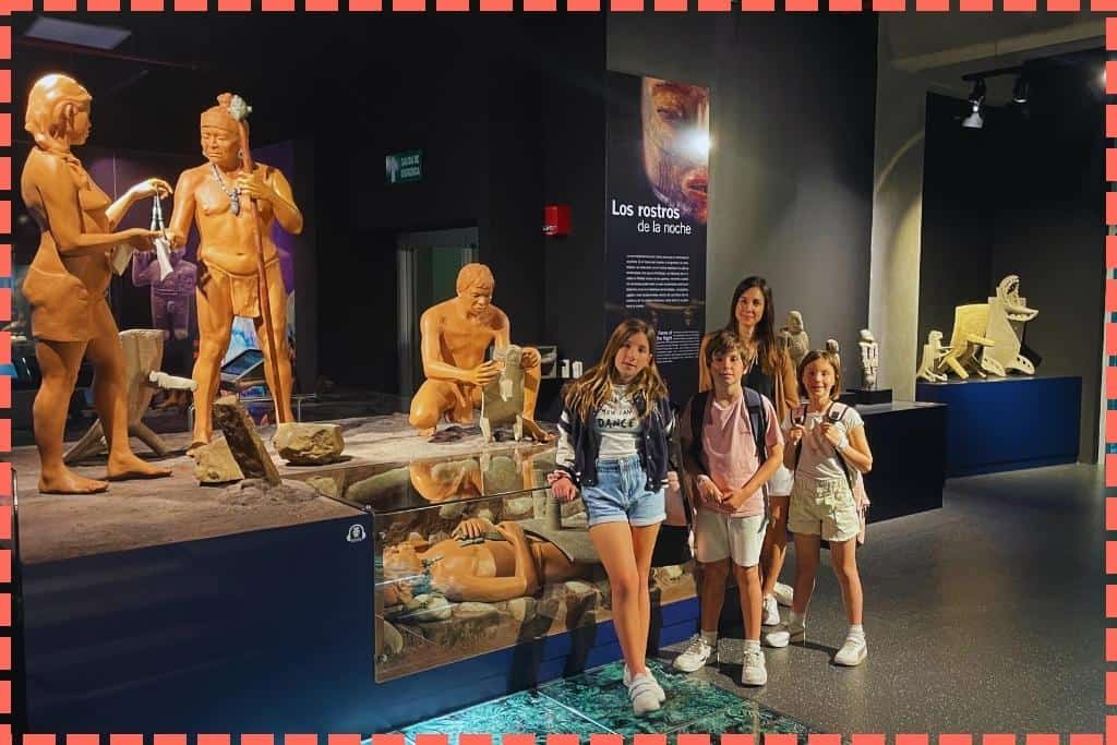 Tere Watson y sus tres hijos explorando la sala 'La Noche' en el Museo del Jade en San José, Costa Rica, rodeados de figuras que representan rituales chamánicos y funerarios, sumergidos en el aprendizaje cultural y la historia de la región