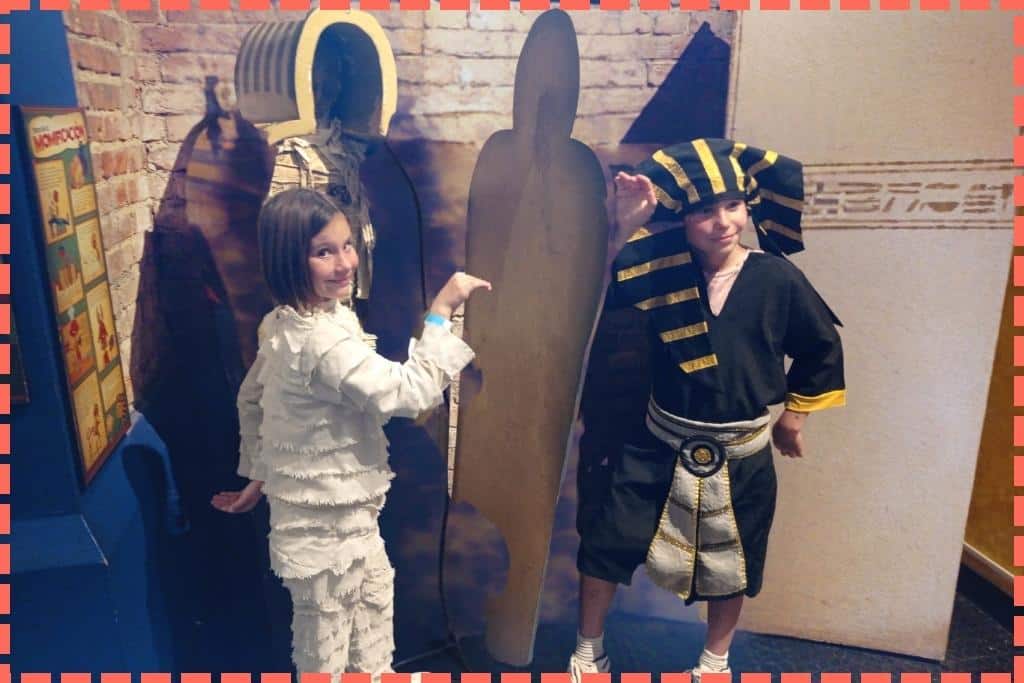 Ian y Vicky, disfrazados con atuendos egipcios, bailando y riendo en la sala del Antiguo Egipto en el Museo de los Niños. Los hermanos disfrutan de una experiencia lúdica y educativa, sumergiéndose en la cultura egipcia antigua a través de la danza y el juego, en una actividad que combina diversión y aprendizaje de la historia.