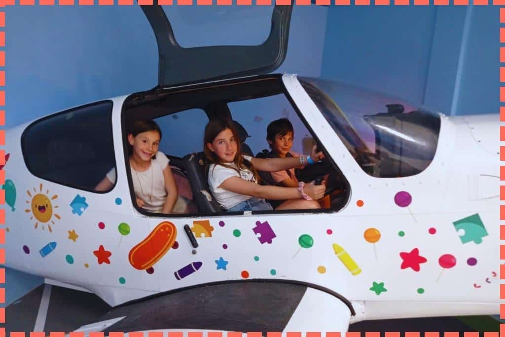 Tres niños dentro de una avioneta de exhibición en el Museo de los Niños, fingiendo ser pilotos y viajeros, disfrutando de una experiencia imaginativa y emocionante de 'volar' en una aeronave.