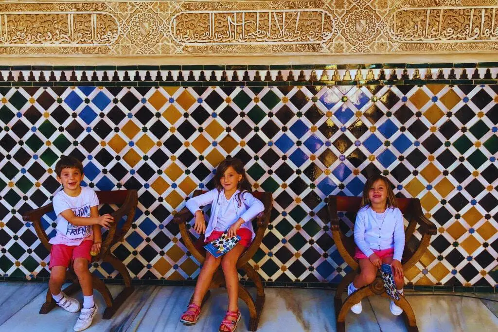 Los 3 hijos mayores de Tere Watson en la Alhambra. Sentados en sillas de la época y los mosaicos de telón de fondo. Disfrutando de unas vacaciones culturales en España.