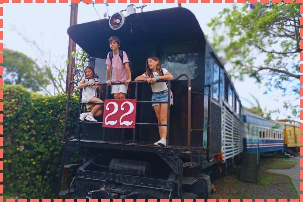 Tres niños subidos en un antiguo tren en exhibición, explorando y disfrutando de la experiencia de estar a bordo de un tren histórico, un recorrido divertido y educativo para los pequeños aventureros.
