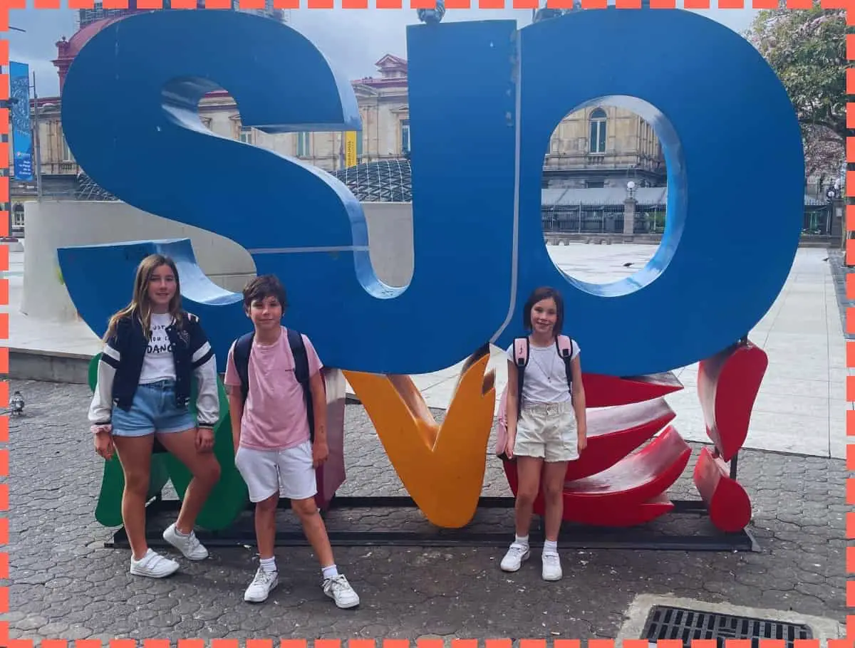 Sofía, Ian y Vicky, hijos de Tere Watson, posando para una foto con el icónico letrero 'SJO Vive!' en la Plaza de la Cultura de San José, Costa Rica. Esta imagen captura un momento memorable de su viaje, simbolizando la vibrante energía y el espíritu de la capital costarricense.