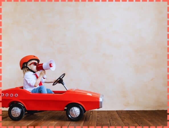 Niño con megáfono conduciondo su coche rojo.