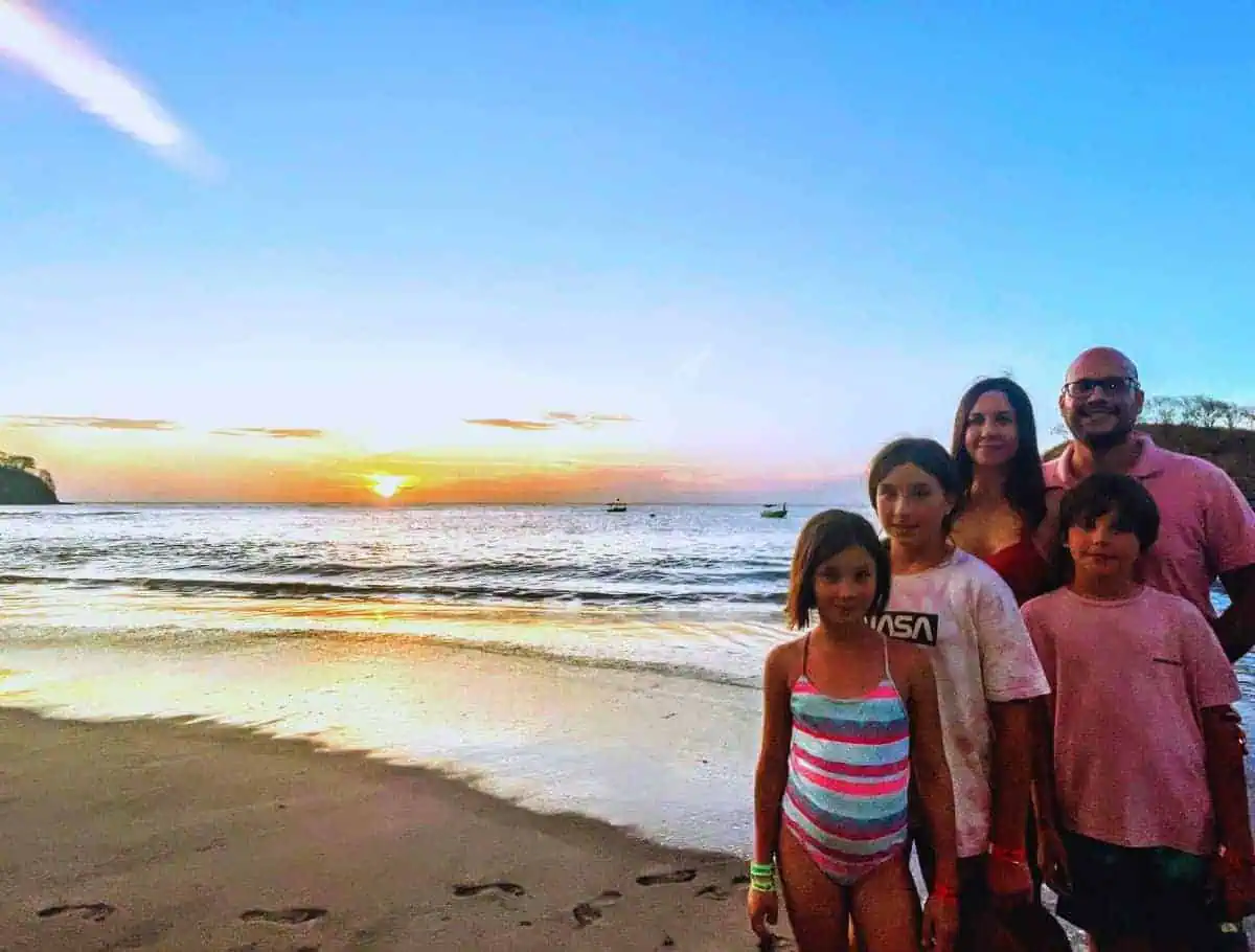 Familia Watson posando para la foto en la Playa Bahía de los Piratas en Costa Rica, disfrutando de un hermoso atardecer con un islote pintoresco al fondo.