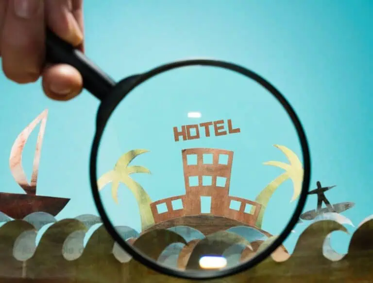 Imagen de una lupa sobre un hotel de carton para la página de buscadores de hoteles.